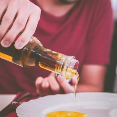 Man pouring olive oil onto a plate indoors, perfect for culinary and healthy eating themes.