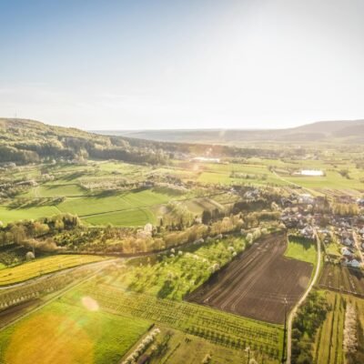 Scenic aerial view of a sunlit countryside village surrounded by green fields.
